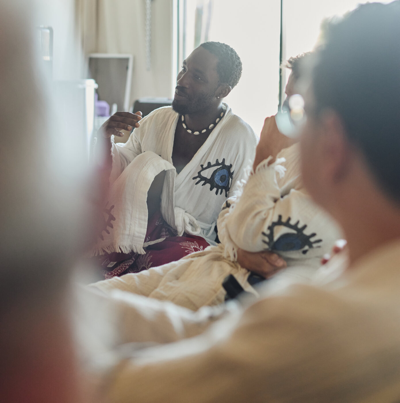 A man in a white robe with an eye motif speaking in a small circle of attendees.
