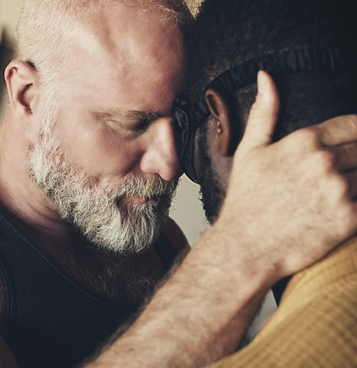 Two men holding each other forehead-to-forehead, eyes closed, in a moment of tender connection.