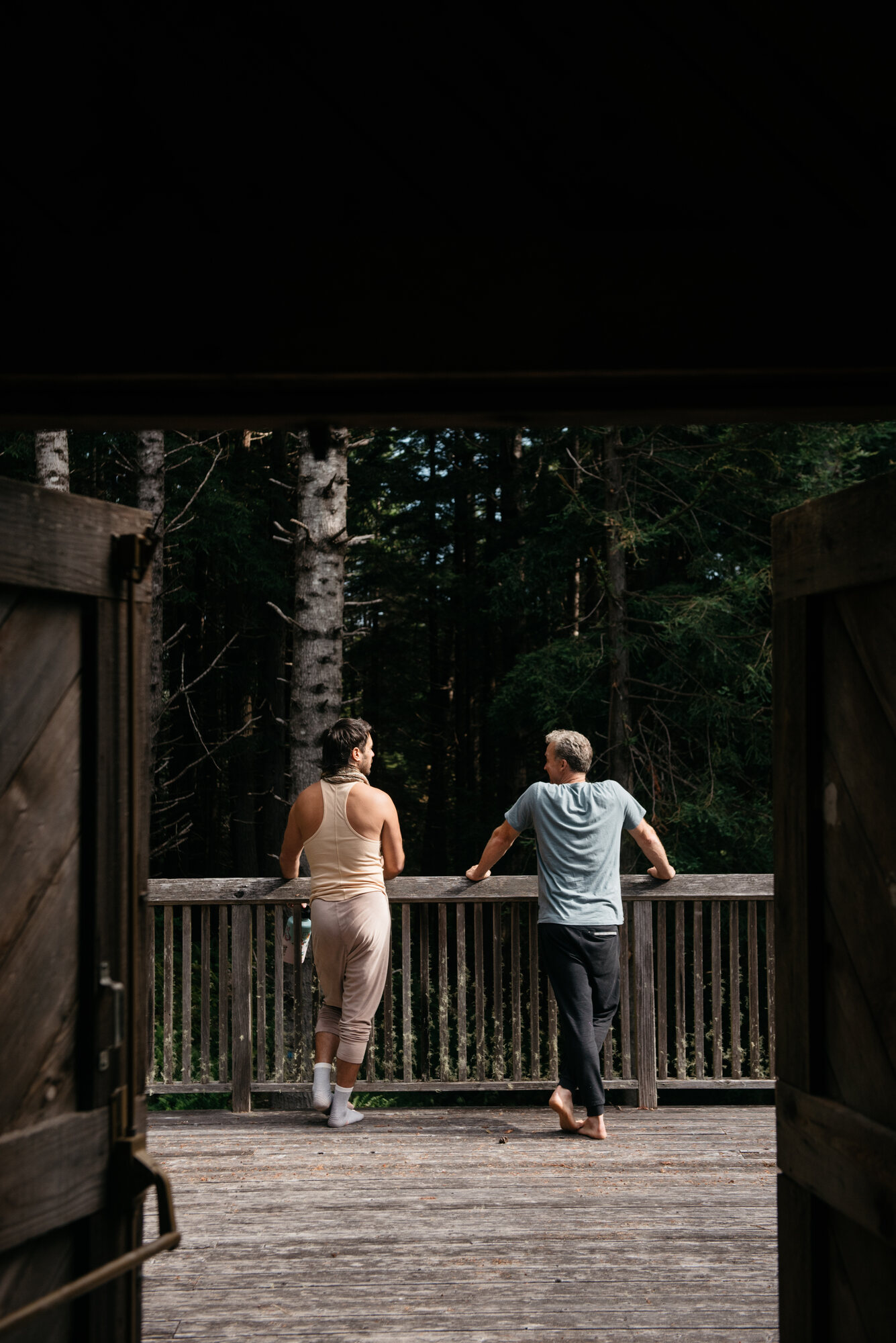 Men standing shoulder-to-shoulder around a roaring campfire in the redwoods at night, arms over each other's backs.