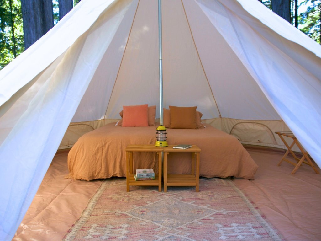The interior of a glamping bell tent at Spirit Camp — soft linens, lantern, redwood beyond the canvas.